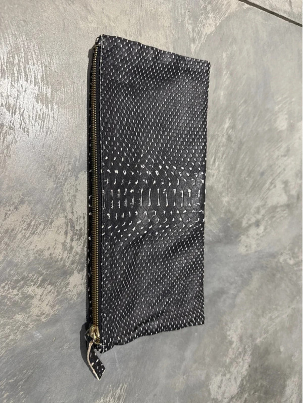 Clare V. foldover zip clutch in a black and white snake-embossed leather pattern